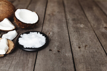 Broken coconuts on gray wooden background. White fresh pulp on black plate