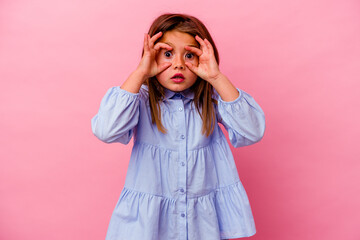 Little caucasian girl isolated on pink background  keeping eyes opened to find a success opportunity.