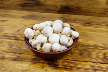 Fresh champignon mushrooms in ceramic bowl on the wooden table
