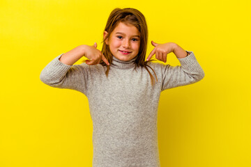 Little caucasian girl isolated on yellow background surprised pointing with finger, smiling broadly.