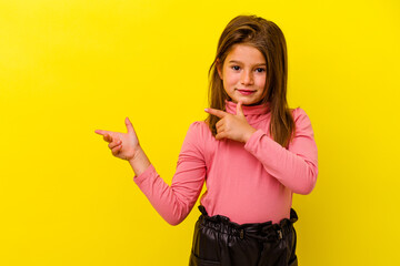 Little caucasian girl isolated on yellow background pointing with forefingers to a copy space,...