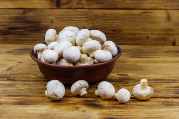 Fresh champignon mushrooms in ceramic bowl on the wooden table
