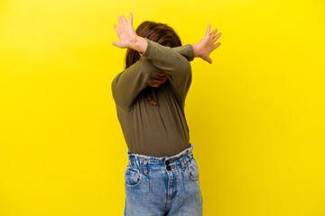 Little caucasian girl isolated on yellow background keeping two arms crossed, denial concept.