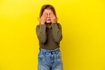 Little caucasian girl isolated on yellow background afraid covering eyes with hands.