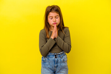 Little caucasian girl isolated on yellow background praying, showing devotion, religious person...
