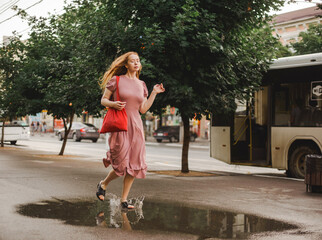 Young beautiful red-haired long-haired woman in a summer pink dress walks through the streets of a...