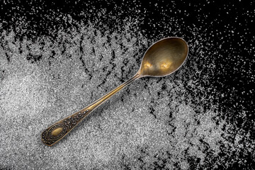Vintage spoon and sprinkled sugar on a black table.