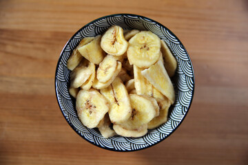 Banana chips in a beautiful ceramic bowl on a wooden table. Vegan snack. Healhty food. Vegetarian diet.