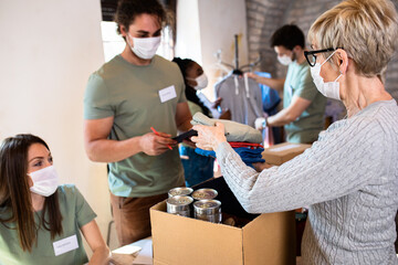 Group of volunteers with face mask working in community charity donation center.