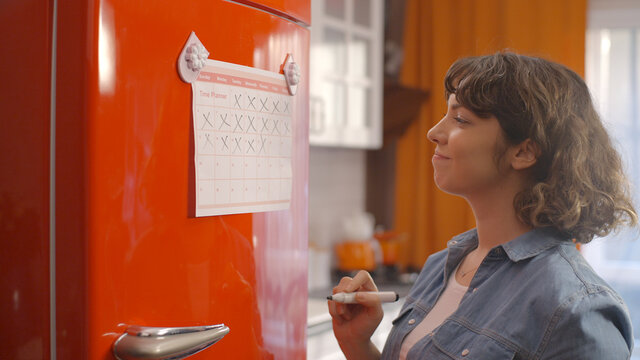 The woman who follows the flow of time on his diet program in the refrigerator. The young woman counts his schedule and marks it with a pencil.