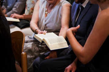 In der Kirche sitzen viele Leute, eine Frau übergibt einem Mann eine Bibel. Alle sind schick...
