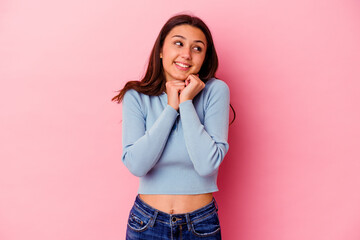 Young Indian woman isolated on pink background keeps hands under chin, is looking happily aside.