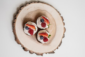 red cream cupcakes with strawberries and blueberries on natural wood coasters