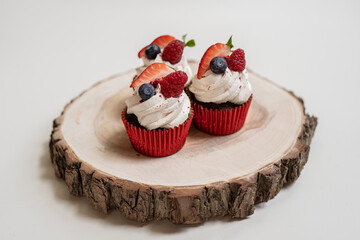 red cream cupcakes with strawberries and blueberries on natural wood coasters