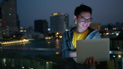 Asian male wear jacket and glasses casual cloth working type data coding programer with laptop working at night with bokeh light night from city building cityscape background - Powered by Adobe