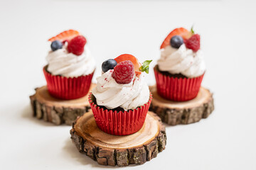 red cream cupcakes with strawberries and blueberries on natural wood coasters - 420305659
