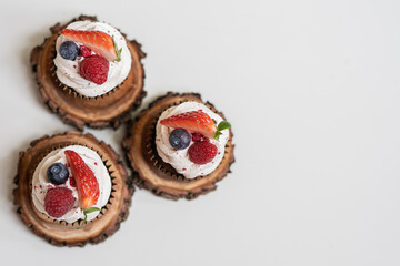 red cream cupcakes with strawberries and blueberries on natural wood coasters