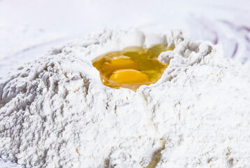 Baking scenery with a heap of wheat white flour for kneading dough for pasta or pizza with a raw egg on top. Close up. Homemade baking concept.