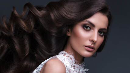 Fototapeta premium Beautiful brown-haired girl with a perfectly curls hair, and classic make-up. Beauty face and hair.