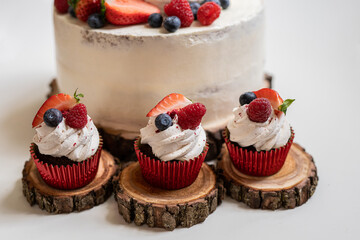 red cream cupcakes with strawberries and blueberries on natural wood coasters