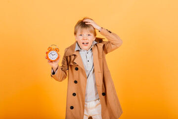 Shocked boy holding clock alarm, copy space. Kid isolated over yellow background. Time for school.