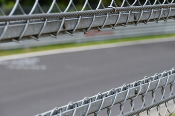 Steel safety fence around the race track and empty road in background