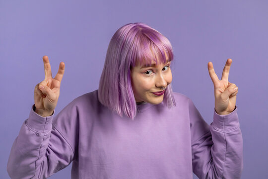 Pretty woman with dyed purple hair showing with hands and two fingers air quotes gesture, bend fingers isolated over violet background. Not funny, irony and sarcasm concept.