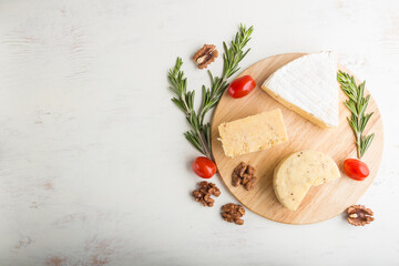 Cheddar and various types of cheese with rosemary and tomatoes on wooden board on a white background . Top view, copy space.