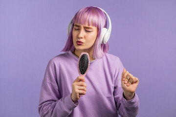 Young pretty woman with violet hairstyle singing and dancing with hair brush or comb instead...
