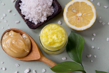 Natural cosmetic scrub with sea salt, honey and lemon in a glass jar on a deoevyan stand, next to a half lemon, a wooden spoon with honey, a jar of sea salt and pieces nearby, close-up