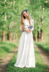 Fototapeta na wymiar Smiling young woman in white wedding dress with flowers enjoying a summer day in beautiful nature