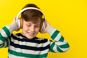 Little redhead boy isolated on yellow background listening music