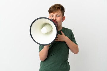 Little redhead boy isolated on white background shouting through a megaphone with surprised expression