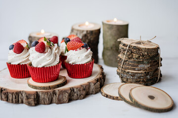 red cream cupcakes with strawberries and blueberries on natural wood coasters