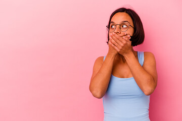 Young mixed race woman isolated on pink background thoughtful looking to a copy space covering mouth with hand.