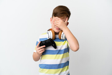 Little redhead boy holding a game pad isolated on white background covering eyes by hands. Do not want to see something