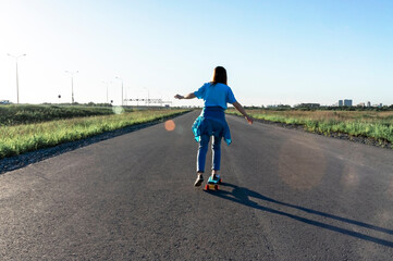 Obraz premium Skater caucasian Young woman from the back in blue jeans and a t-shirt skateboarding on the road in summer, active lifestyle, outdoor activities