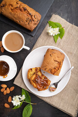 Homemade cake with raisins, almonds, soft caramel and a cup of coffee on a black concrete background. top view, close up.