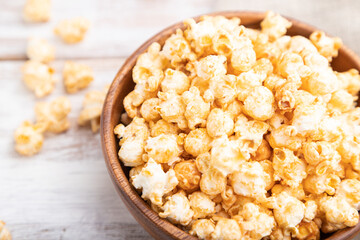 Popcorn with caramel in wooden bowl and a cup of coffee on a white wooden background. Side view, selective focus.