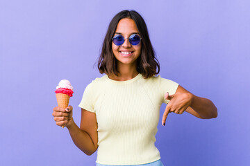 Young mixed race woman eating an ice cream points down with fingers, positive feeling.