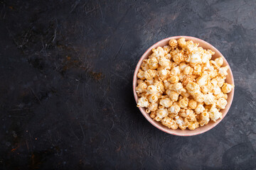 Popcorn with caramel in ceramic bowl on a black concrete background. Top view, copy space.