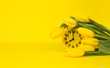 A bouquet of yellow tulips with a yellow alarm clock on a yellow background. Spring morning. Copy space. Space for text