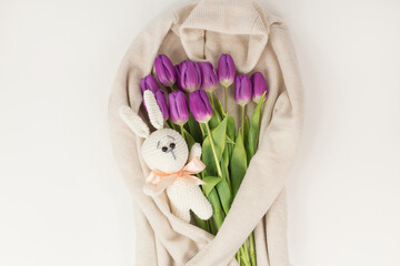 A bouquet of tulips and a knitted bunny on the background of a cream knitted sweater, a top view of a bouquet of tulips for women's day, the concept of spring flowers