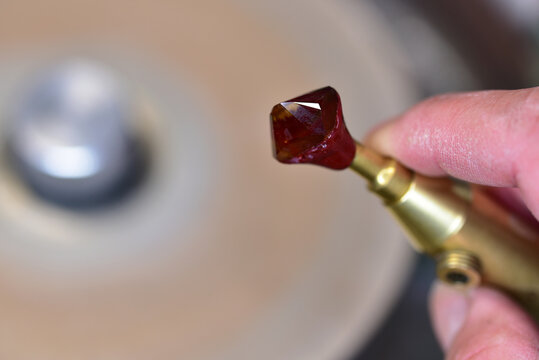 Craftsman's hand holding metal dop with citrine stone during faceting process.