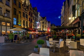 Fototapeta na wymiar Old cozy narrow street with tables of restaurant in historic city center of Antwerpen (Antwerp), Belgium. Night cityscape of Antwerp. Architecture and landmark of Antwerpen