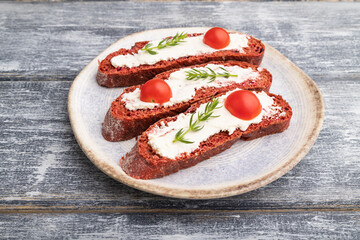 Red beet bread sandwiches with cream cheese and tomatoes on gray wooden background. Side view.