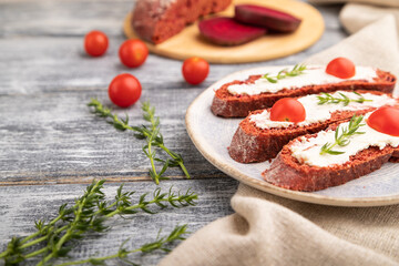Red beet bread sandwiches with cream cheese and tomatoes on gray wooden background. Side view, selective focus.