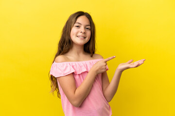 Little caucasian girl isolated on yellow background holding copyspace imaginary on the palm to insert an ad