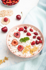 Rice flakes porridge with milk and strawberry in ceramic bowl on white concrete background. Side view.
