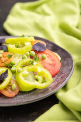 Vegetarian salad from green pea, tomatoes, pepper and basil on a black concrete background. Side view, selective focus.
